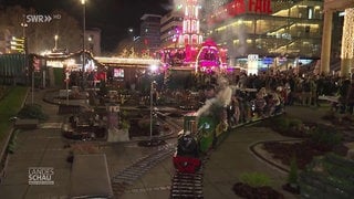 Kinder und Erwachsene fahren auf einer kleinen Lok durch eine Miniaturlandschaft auf dem Stuttgarter Weihnachtsmarkt