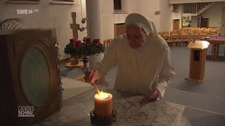 Ordensschwester Walburgis sündet eine Kerze in der Kirche an