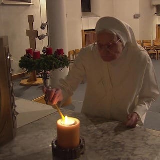 Ordensschwester Walburgis sündet eine Kerze in der Kirche an