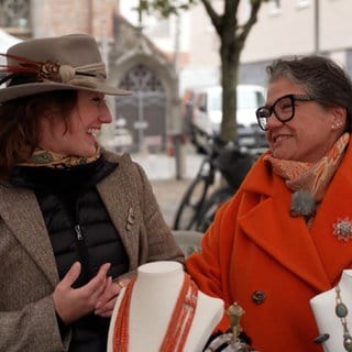 Zwei Frauen lächeln sich auf dem Flohmarkt an