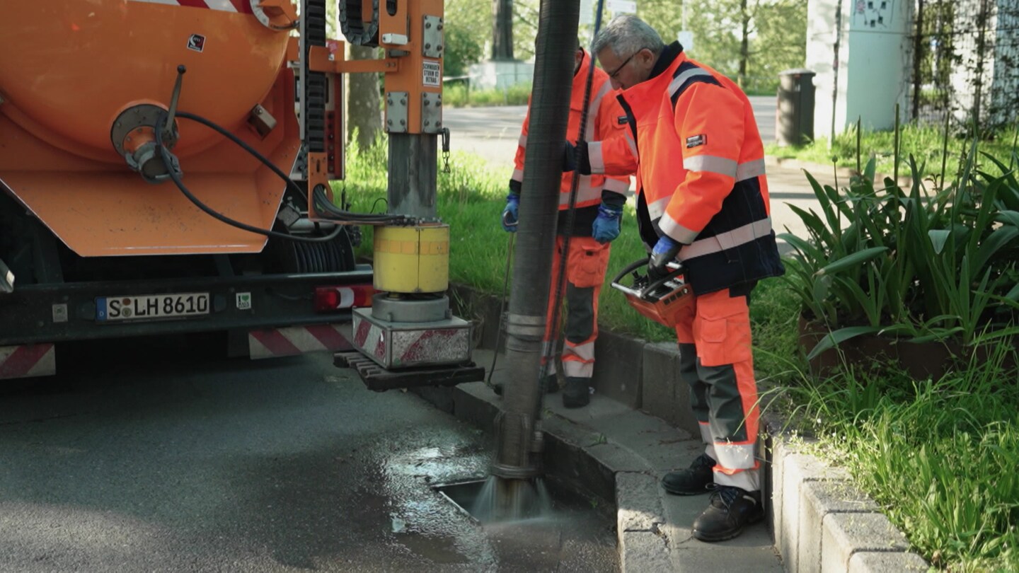 Ein Mitarbeiter der Kanalreinigung reinigt einen Kanaleingang mit einem großen Schlauch