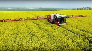 Landmaschine mit weit ausladender Spritzmittel-Vorrichtung fährt durch ein blühendes Rapsfeld