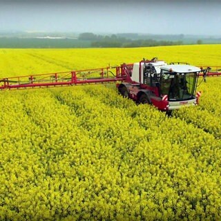 Landmaschine mit weit ausladender Spritzmittel-Vorrichtung fährt durch ein blühendes Rapsfeld