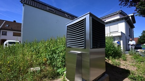 Eine Wärmepumpe steht im Garten vor einer Garage