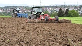 Landwirte bearbeiten mit Hilfe von Traktoren ein Feld.