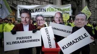 Eine Protestaktion von Deutscher Umwelthilfe und BUND bei der Teilnehmer Masken mit Bildern von Politikern tragen 