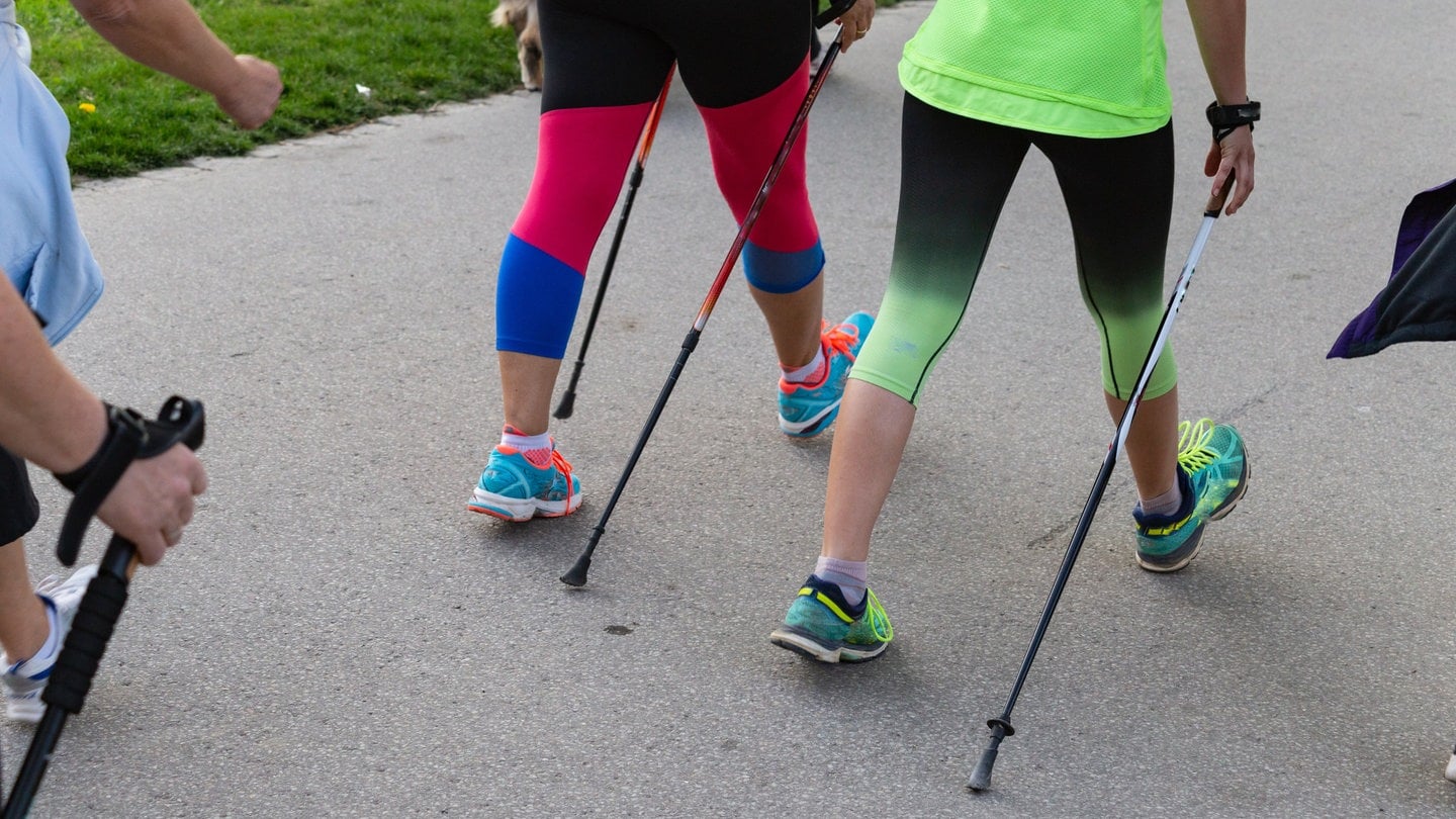 Zwei Personen laufen mit Nordic Walking Stöcken auf einem Weg