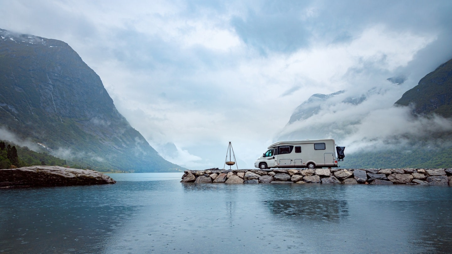 Ein Wohnmobil steht an der Küste. Im Hintergrund sind Berge zu sehen.