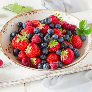 In einer weißen Schale liegen verschiedene Beerensorten: Heidelbeeren, Erdbeeren und Himbeeren