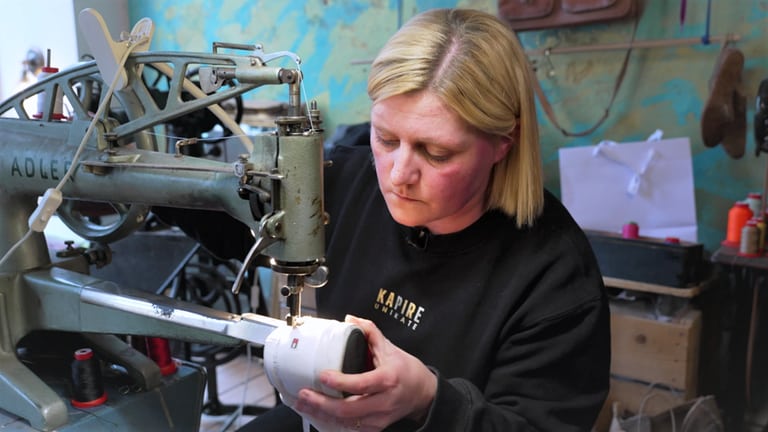 Die Besitzerin einer Sneaker-Reparatur-Werkstatt sitzt an einer Industrienähmaschine und näht einen weißen Sneaker.