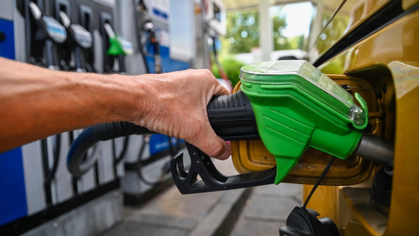 Eien Hand hält an einer Zapfsäuale an der Tankstelle einen grünen Tankrüssel in die Tankklappe, und betankt das Auto mit Kraftstoff.