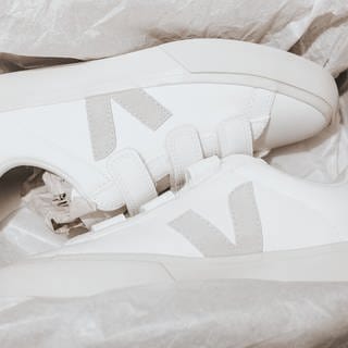 In einem Schuhkarton liegen ein Paar weiße Sneaker von der nachhaltigen Marke Veja. Die nachhaltigen Sneaker haben ein graues Veja-Logo an der Seite