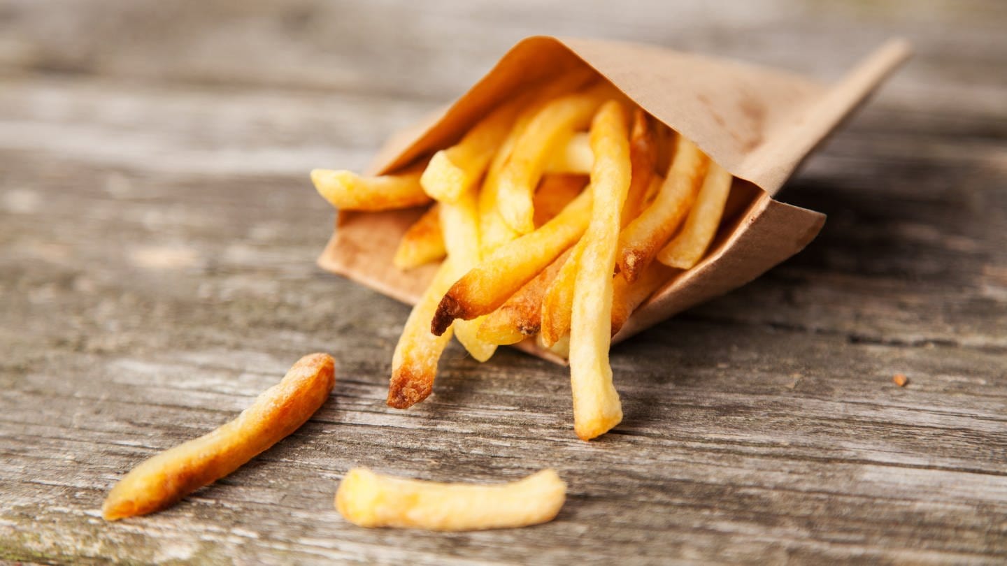 Auf einem hölzernen Untergrund liegt eib´ne halb ausgekippte braune Schachtel Pommes.