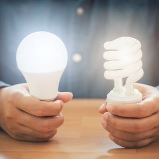 Eine Person sitzt an einem Holztisch und hält jeweils eine LED-Lampe in der Hand, die leuchten.