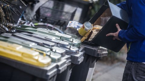 Ein junger Mann schüttet Abfall in eine Mülltonne. Je nach Wohnort bezahlen Haushalte in Deutschland nach einer Studie sehr unterschiedliche Müllgebühren.