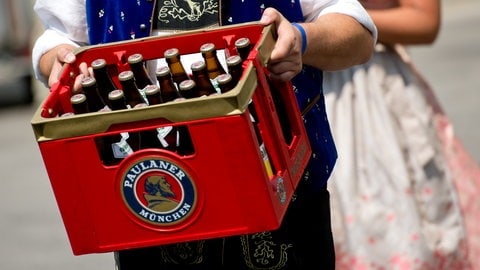 Ein traditionell gekleideter mann trägt einen Kasten Paulaner Weißbier.