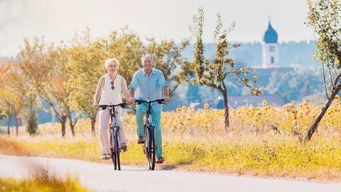 Ein älteres Pärchen fährt einen Feldweg entlang. E-Bikes unterstützen den Fahrer beim Treten. So kann man auch steile Hänge problemlos hoochfahren.