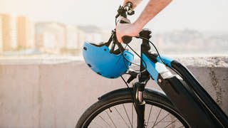 Ein Mann fährt ein E-Bike. Am Lenker hängt ein blauer Helm.