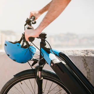 Ein Mann fährt ein E-Bike. Am Lenker hängt ein blauer Helm.