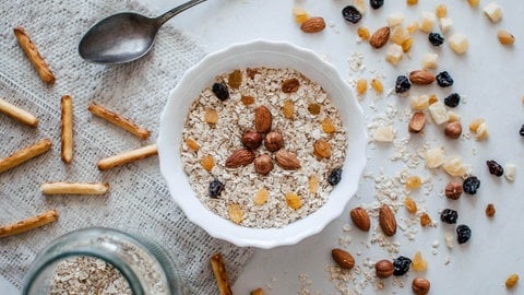 Haferflocken in einer Schüssel mit Mandeln, Haselnüsse und Trockenfrüchte wie Rosinen und Mango.