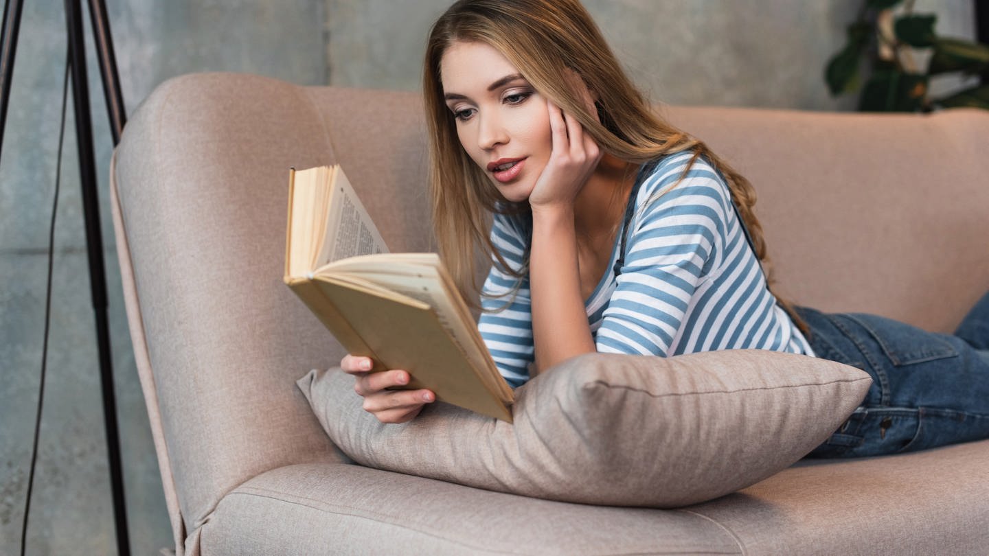 Frau liegt auf einem Sofa und liest ein Buch