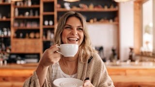 Eine Frau lächelt während sie eine Tasse Kaffee in der Hand hält.