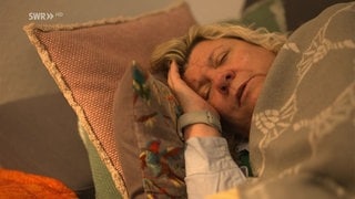 Frau liegt im Bett und hält sich den Kopf