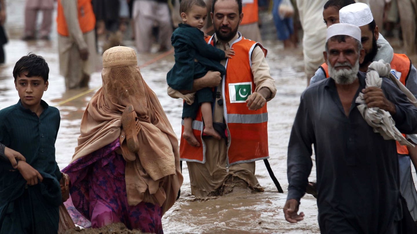 Menschen in Pakistan waten durch die Flut