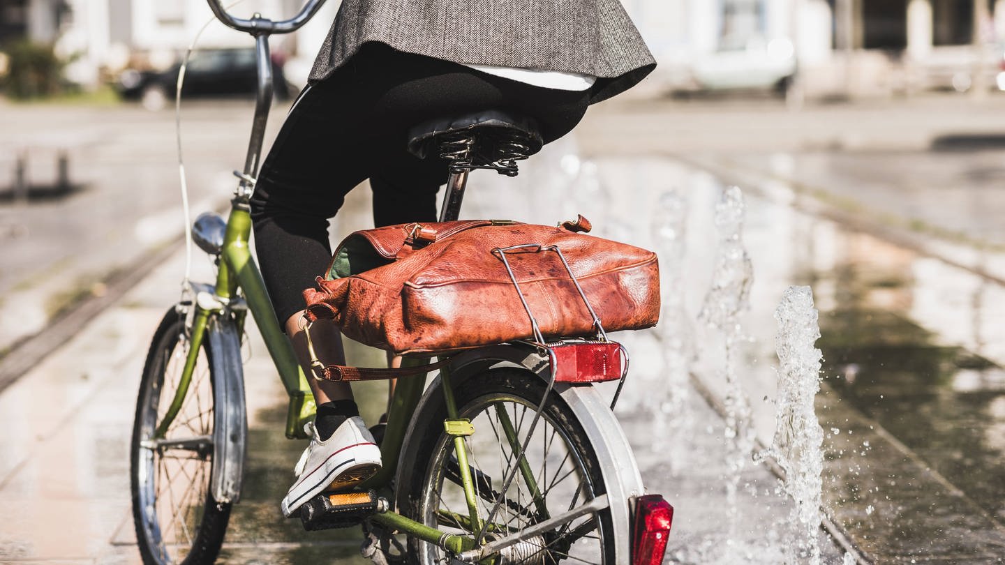 Radfahrerin mit Aktentasche auf dem Gepäckträger: Durch Radfahren kann man seine persönliche Klimabilanz verbessern