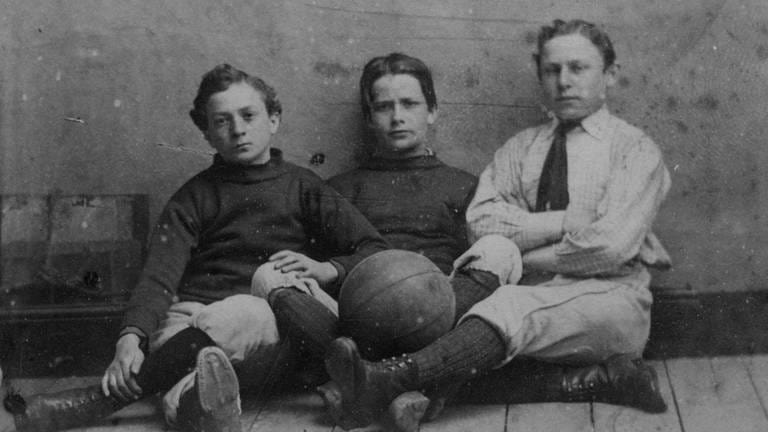 Drei Jungs in Sportkleidung mit Fußball, England um 1885