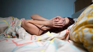 Eine junge Frau liegt wach im Bett: Wer abends zu spät isst, kann Probleme mit dem Einschlafen und Durchschlafen bekommen. Der Magen hat dann noch zu viel zu arbeiten.