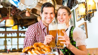 Mann und Frau in Tracht mit je einem Bierglas in der Hand: Deutsche Männer trinken mehr als sechsmal so viel Bier wie die Frauen. Die Gründe sind unklar. Zum einen trinken Männer grundsätzlich mehr Alkohol. Aber beim Bier sind die Unterschiede besonders auffallend.