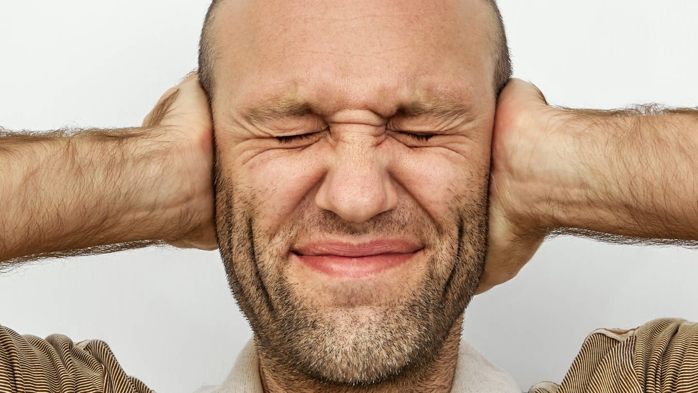 Ein Mann hält sich mit geschlossenen Augen gestresst die Ohren zu: Stresserfahrungen werden in der Großhirnrinde als Gedächtnisspuren abgelegt