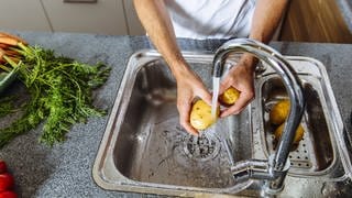 Kartofelln werden unter fließendem Wasser in der Spüle gewaschen: Manches Gemüse oder Obst wir nur wegen des groben Drecks: Es ist einfach blöd, wenn es beim Verzehr von Salat oder Kartoffeln zwischen den Zähnen knirscht. Aber muss Obst und Gemüse aus hygienischen oder gesundheitlichen Gründen gewaschen werden?