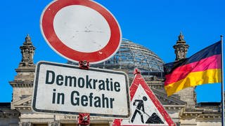 Schild vor der Reichstagskuppel "Demokratie in Gefahr": Deutsche Rechtsextreme und Islamisten nähern sich – trotz großer ideologischer Unterschiede – immer wieder an. Entstehen hier neue Bündnisse? Wie gefährlich ist das für Deutschland?