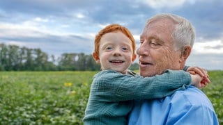 Ein älterer Mann steht am Rand eines Feldes und hält seinen kleinen Enkel auf dem Arm: Für Kinder dauert ein Jahr eine gefühlte Ewigkeit, im Alter geht die Zeit im Nu vorbei. Dieses Phänomen ist inzwischen gut belegt und lässt sich psychologisch erklären.