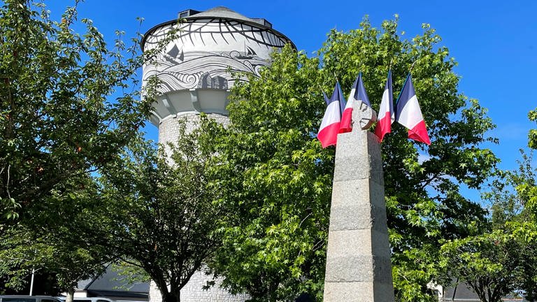 Wasserturm in Damgan. Im Vordergrund ein mit französischen Fahnen geschmücktes Kriegerdenkmal zur Erinnerung an gefallene Soldaten der Gemeinde.