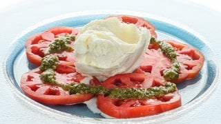 Tomaten mit grünem Pesto und Mozzarella auf einem Teller: Mozzarella ist ein Frischkäse, der bei 70 bis 80 Grad gebrüht wurde. Dieses Brühen sorgt für eine stärkere Verklumpung der Eiweißmoleküle. 