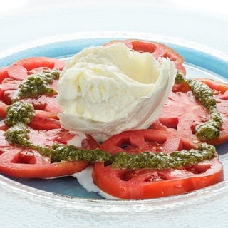 Tomaten mit grünem Pesto und Mozzarella auf einem Teller: Mozzarella ist ein Frischkäse, der bei 70 bis 80 Grad gebrüht wurde. Dieses Brühen sorgt für eine stärkere Verklumpung der Eiweißmoleküle. 