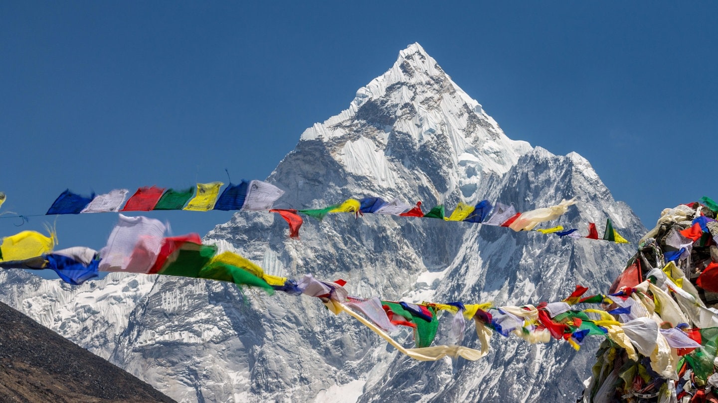 Ama Dablam mit im Wind wehenden buddhistischen Gebetsfahnen am Thokla-Pass auf dem Weg zum Everest-Basislager im Sagarmatha-Nationalpark in Nepal: Heute vermisst man Berge mit Satelliten und GPS, aber schon früher gab es gute Methoden zur Vermessung von Berghöhen.