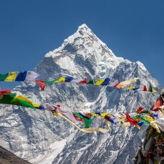 Ama Dablam mit im Wind wehenden buddhistischen Gebetsfahnen am Thokla-Pass auf dem Weg zum Everest-Basislager im Sagarmatha-Nationalpark in Nepal: Heute vermisst man Berge mit Satelliten und GPS, aber schon früher gab es gute Methoden zur Vermessung von Berghöhen.