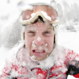 Einschneiter junger Mann mit Schneebrille und Schnee auf der Kleidung: Das Gesicht ist abgehärtet, weil weite Teile des Gesichts kaum behaart sind. Das Gesicht ist daher nicht so kälteempfindlich wie der Rest des Körpers und wir bekommen dort auch keine Gänsehaut. Das Gesicht is die letzte Stelle des Körpers, die wir im Winter verhüllen. 