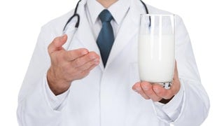 Arzt zeigt auf ein Glas Milch: Stimmt es, dass man Antibiotika nicht mit Milch einnehmen sollte?