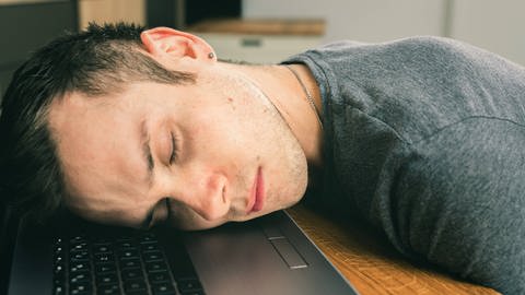 Ein junger Mann schläft auf seinem Laptop.
