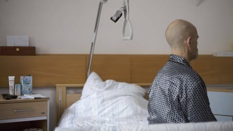 Mann sitzt seitlich abgewandt auf Krankenhausbett: Wenn keine Möglichkeit zur ambulanten Palliativversorgung vorhanden ist, bleibt nur das Sterben im Krankenhaus