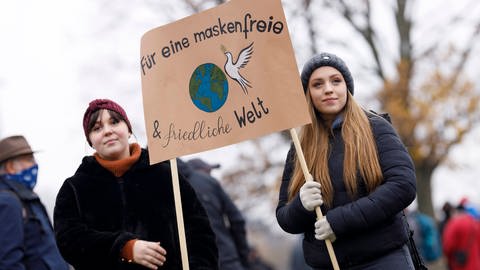 Demonstrantinnen auf einer Düsseldorfer Querdenken-Demo gegen das Tragen von Masken im Dezember 2020, sie halten ein Plakat hoch mit der Aufschrift: "Für eine maskenfreie und friedliche Welt"