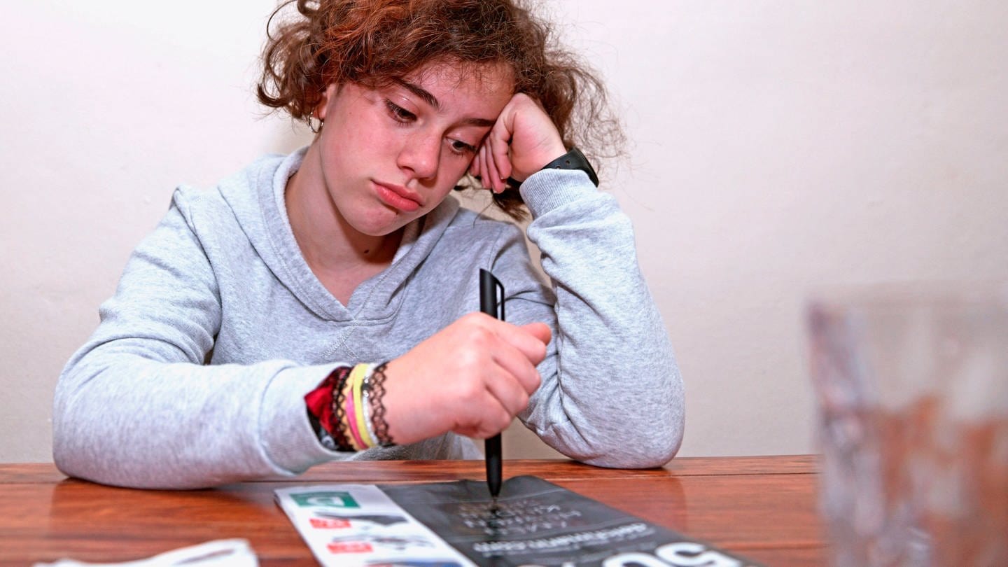 Ein Schulkind muss wegen der Corona-Pandemie Unterricht von Zuhause aus machen, es schaut traurig und gelangweilt