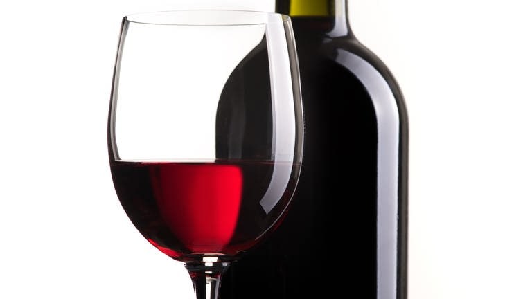 Rotweinglas und Flasche vor weißem Hintergrund
