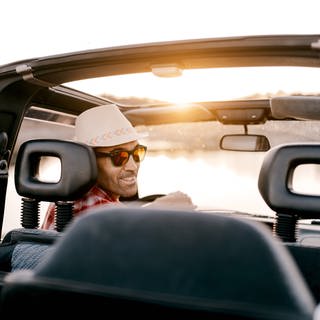 Mann mit Sonnenhut am Steuer eines Autos