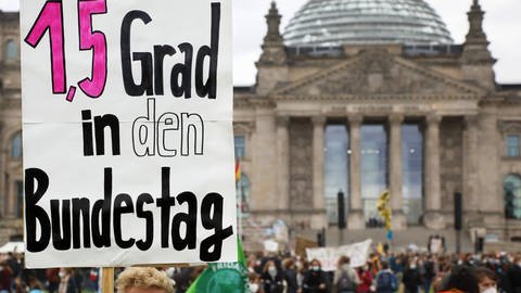Ein Klima-Demonstrant hält ein Schild vor dem Reichstagsgebäude in Berlin in die Höhe.